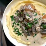 A white bowl with mash, chicken in mushroom sauce topped with fresh parsley