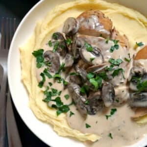 A white bowl with mash, chicken in mushroom sauce topped with fresh parsley