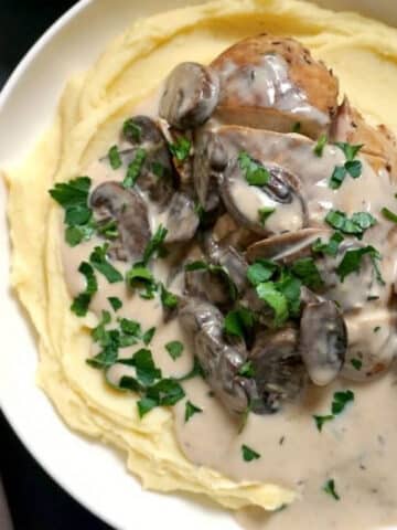 A white bowl with mash, chicken in mushroom sauce topped with fresh parsley