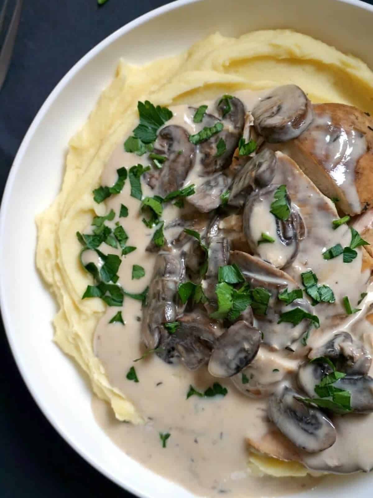 A white bowl with mash, chicken and mushroom sauce.