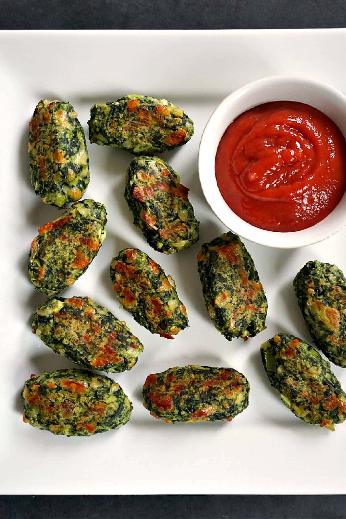 Overhead shoot of a white plate with 11 veggie tots and a ramekin with ketchup