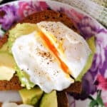 Close-up shoot of a plate with a slice of bread topped with avocado and a poached egg