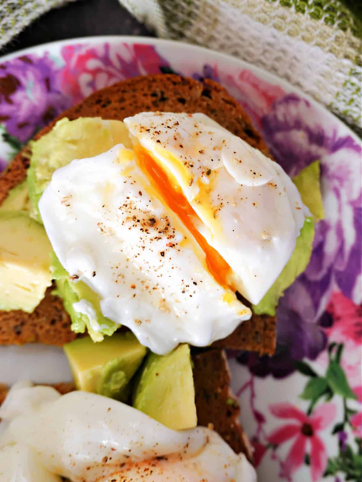 Close-up shoot of a slice of toast with a poached egg on a bed of avocado cubes.