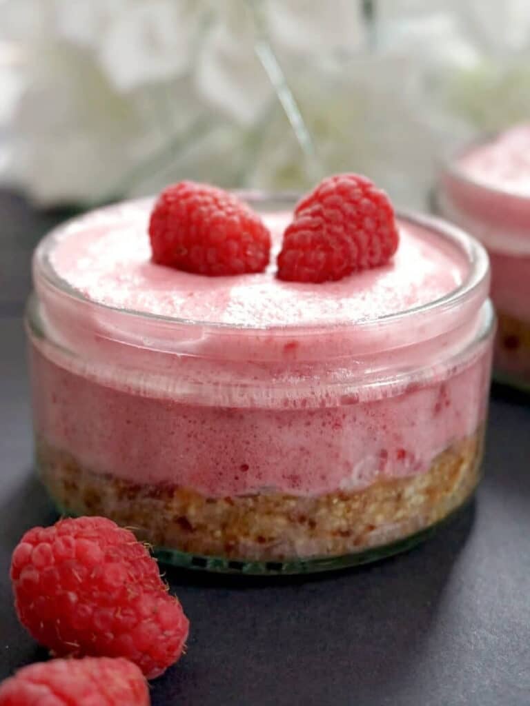 A ramekin with raspberry mousse cheesecake topped with 2 raspberries