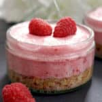 A glass ramekin with raspberry mousse cheesecake topped with 2 raspberries