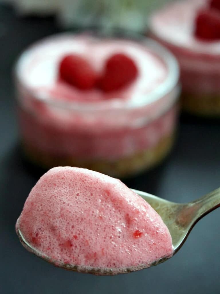 A spoonful of raspberry mousse with a ramekin of cheesecake in the background