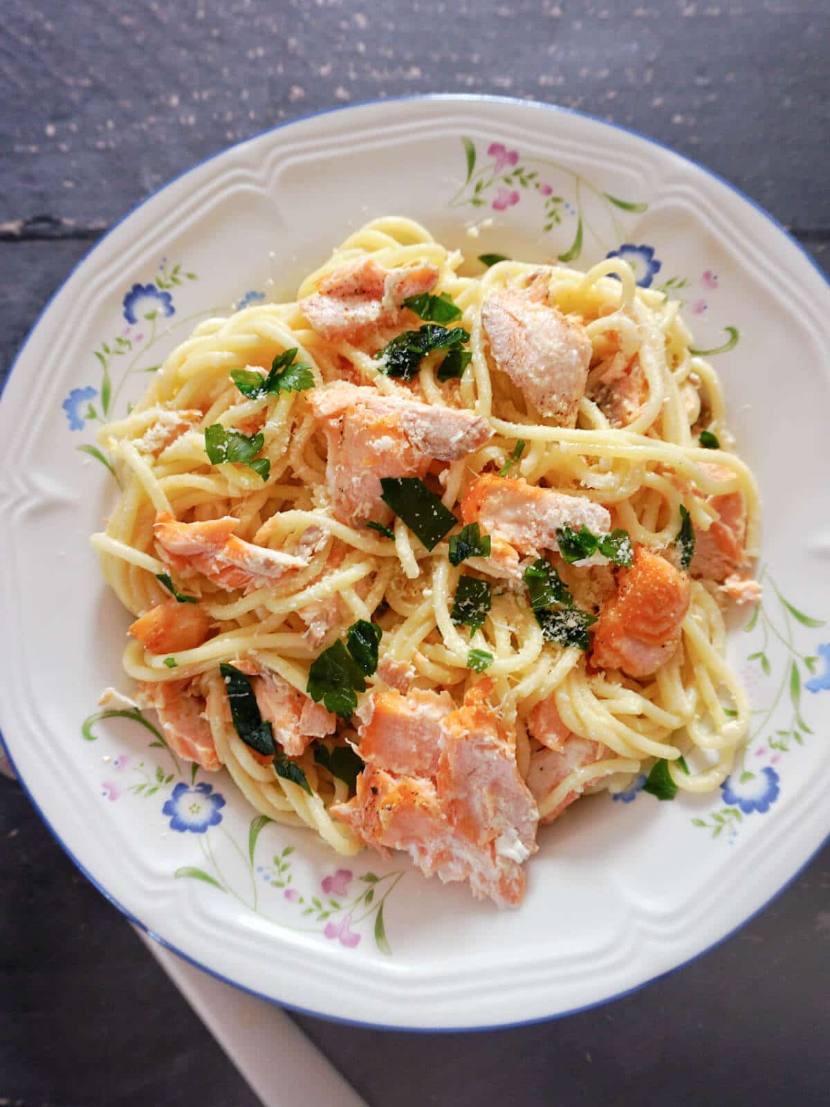 Overhead shot of a white plate with pasta carbonara and salmon flakes