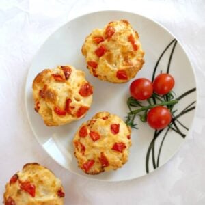 Overhead shoot of a white plate with 3 veggie muffins, 3 cherry tomatoes and a muffin on the side