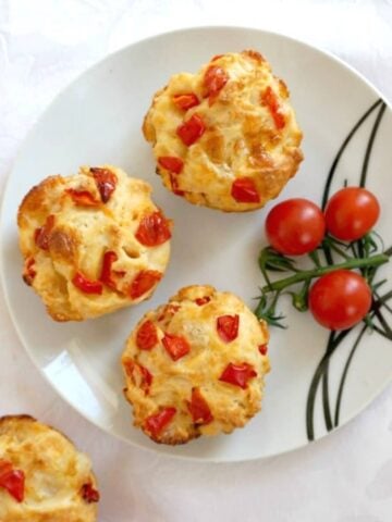 Overhead shoot of a white plate with 3 veggie muffins, 3 cherry tomatoes and a muffin on the side