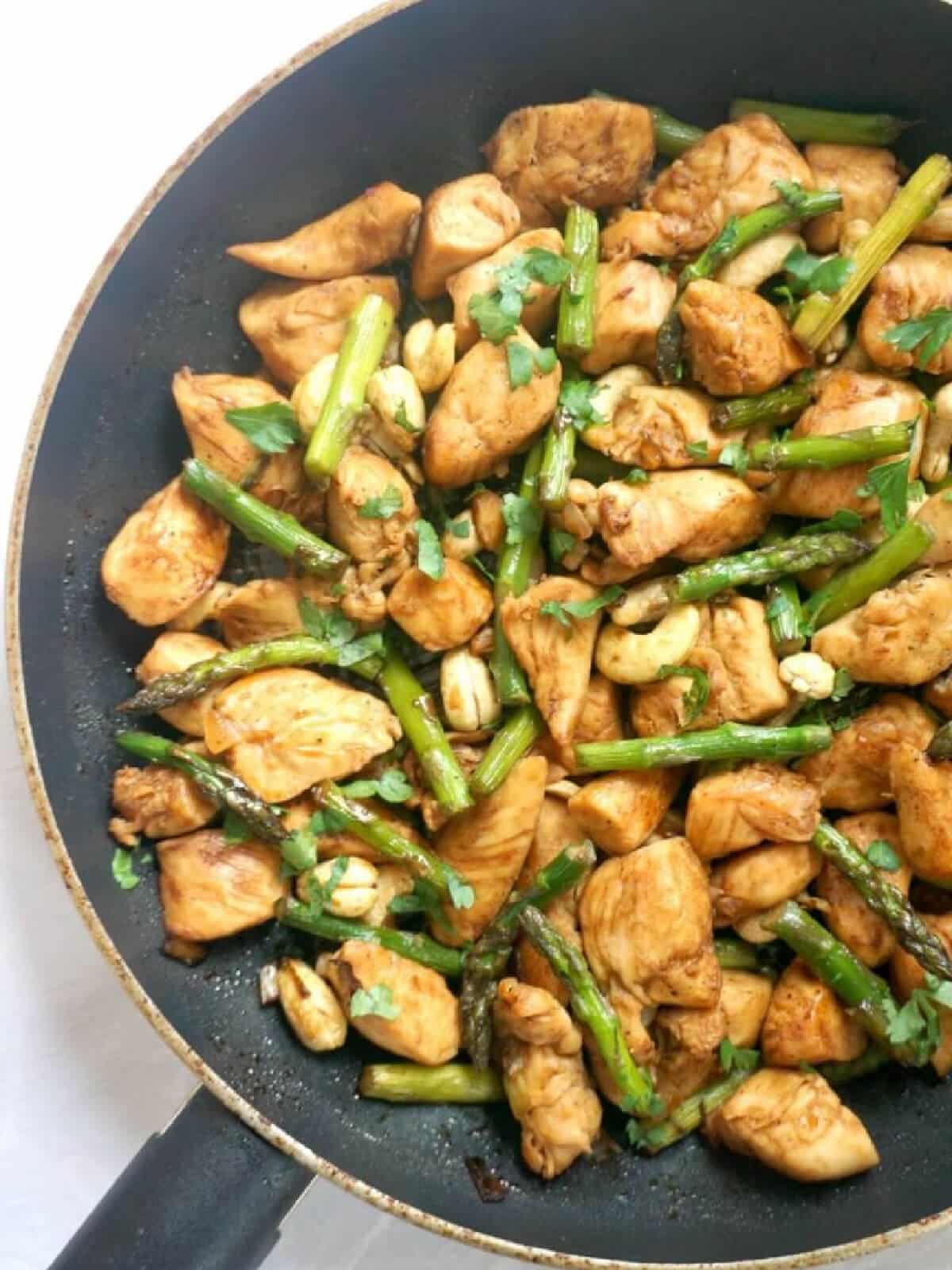 A pan with chicken pieces and asparagus.