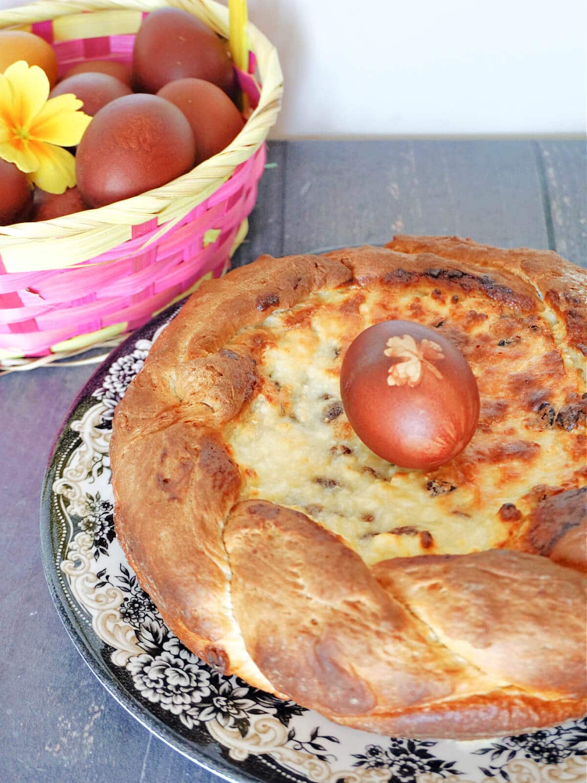 A pasca on a plate with a basket full of dyed eggs at the top.