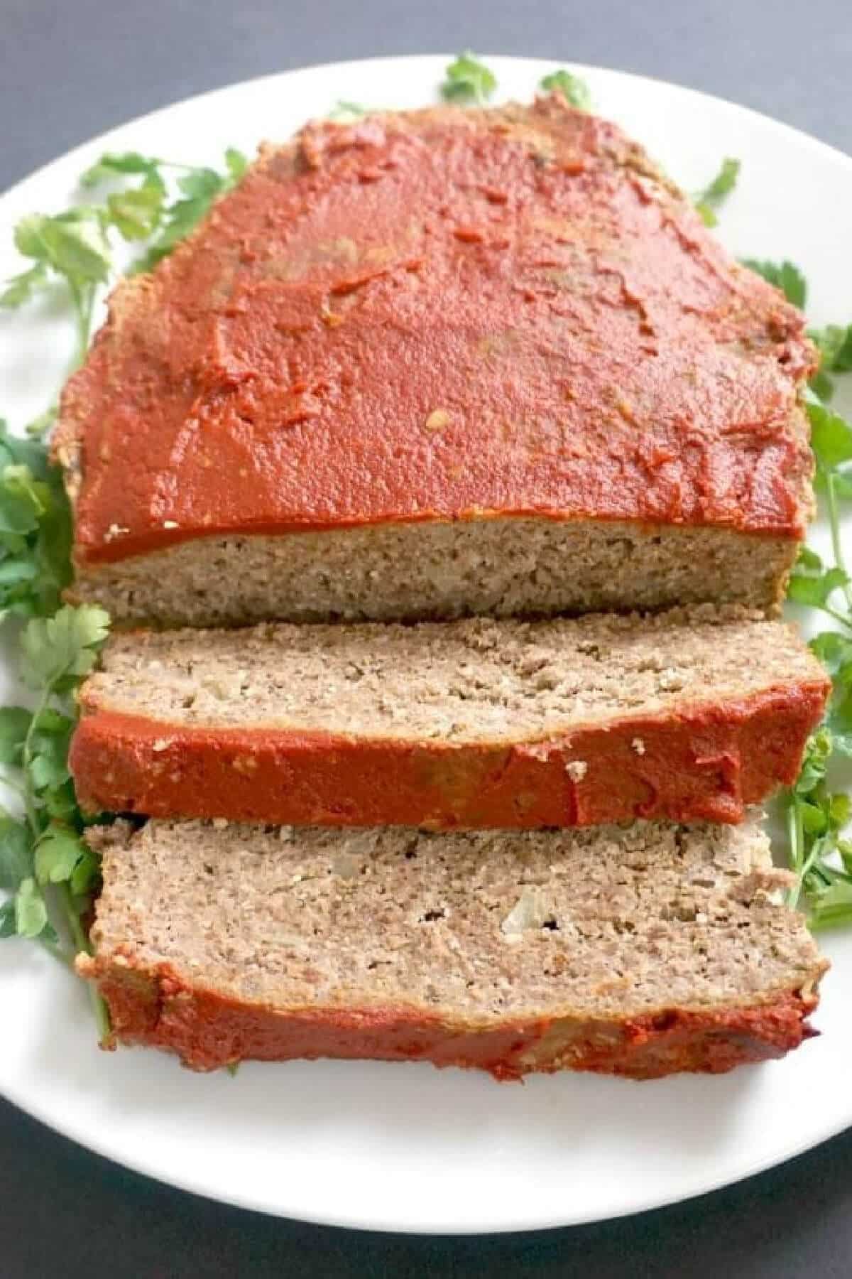 A sliced loaf meat on a white plate decorated with salad leaves.