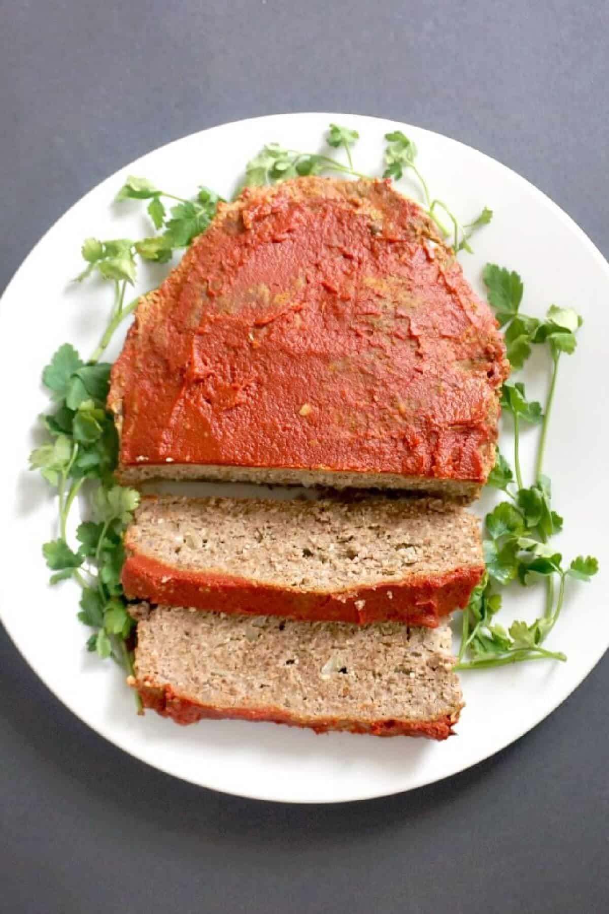 Overhead shoot of a white plate with sliced up meatloaf and salad leaves on the side.