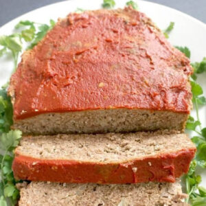 A sliced up meatloaf on a white plate with salad leaves around