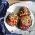 A white plate with 3 stacks of aubergines topped with chopped parsley and parmesan.