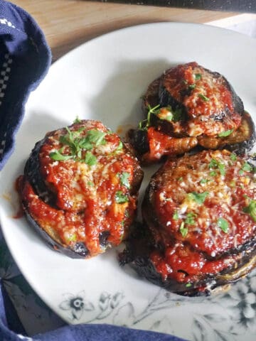 A white plate with 3 stacks of aubergines topped with chopped parsley and parmesan.
