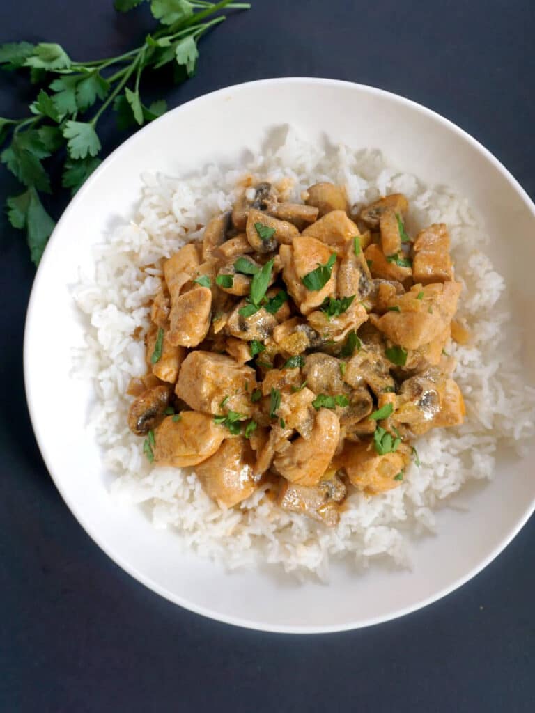 A white plate with chicken stroganoff over a bed of rice