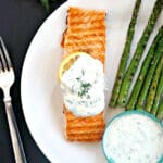 Overhead shoot of a white plate with a salmon fillet and asparagus with a ramekin with yogurt sauce