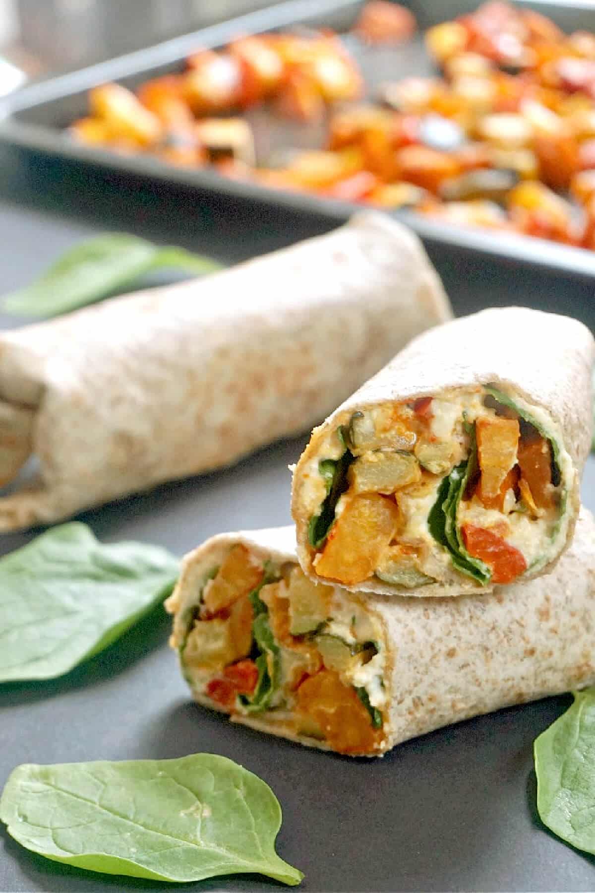 2 halves of a hummus wrap with another wrap in the background and a tray with veggies.