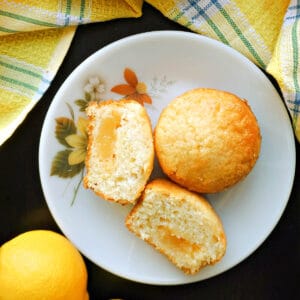 A white plate with 2 halves of a lemon muffin and a whole muffin.