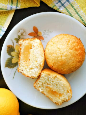 A white plate with 2 halves of a lemon muffin and a whole muffin.