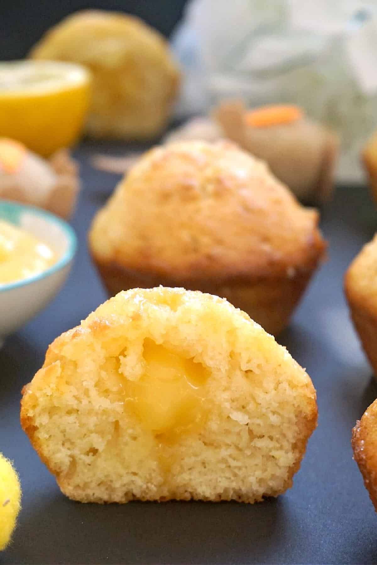 Half of a lemon muffin with lemon curd filling with other muffins in the background