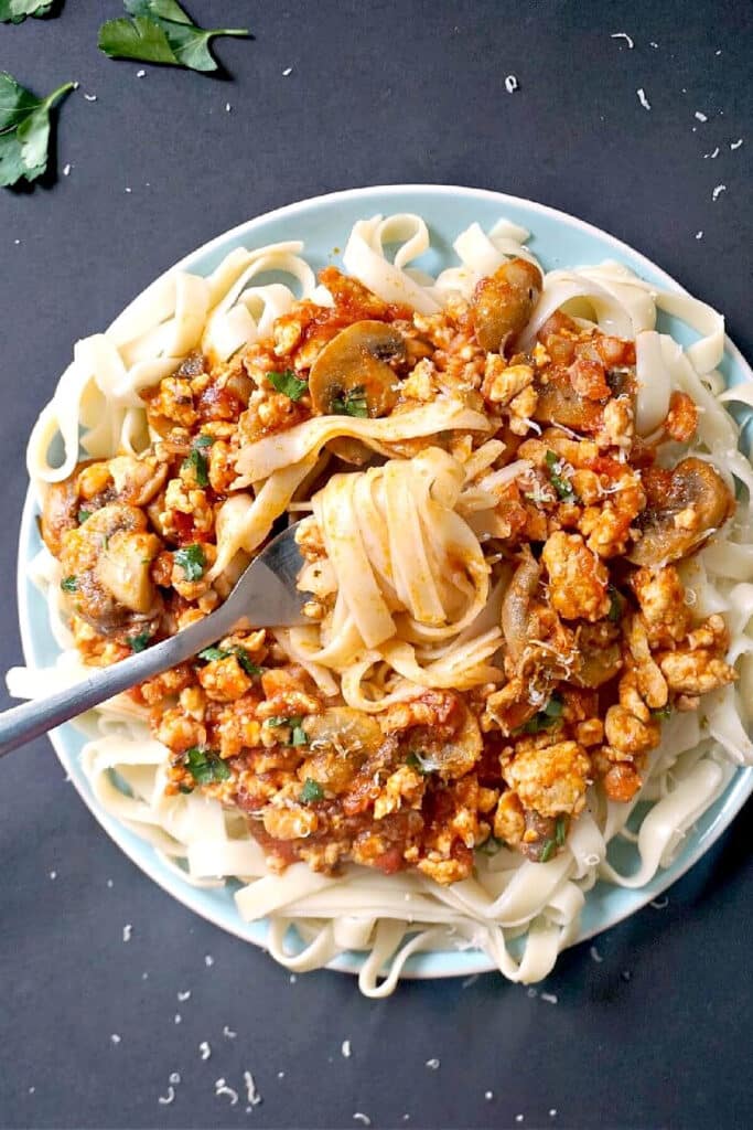 Overhead shoot of a light blue plate with a meat sauce on a bed of tagliatelle
