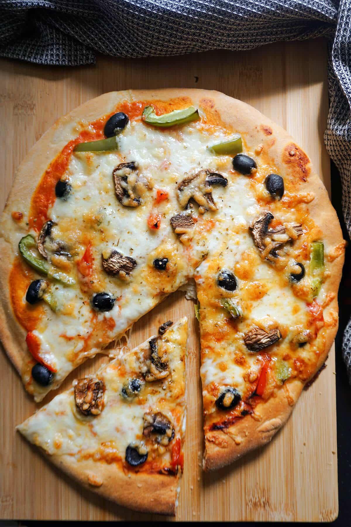 A pizza on a wooden board with a slice cut out of it.