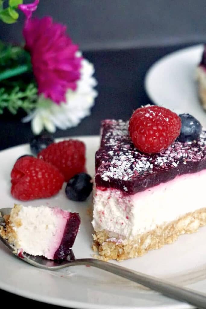 A slice of cheesecake with jelly and fresh berries on a white plate