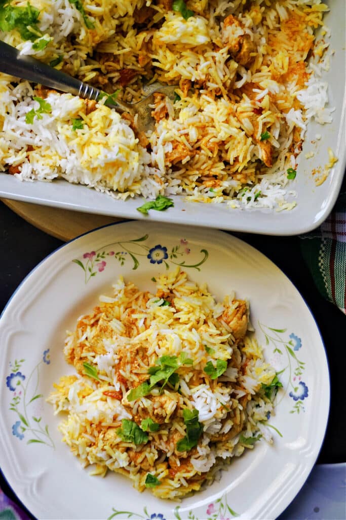 A white plate with chicken biryani and a dish with more biryani