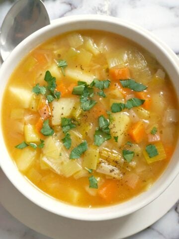 Overhead shoot of a white bowl with leek and potato soup and a spoon next to it