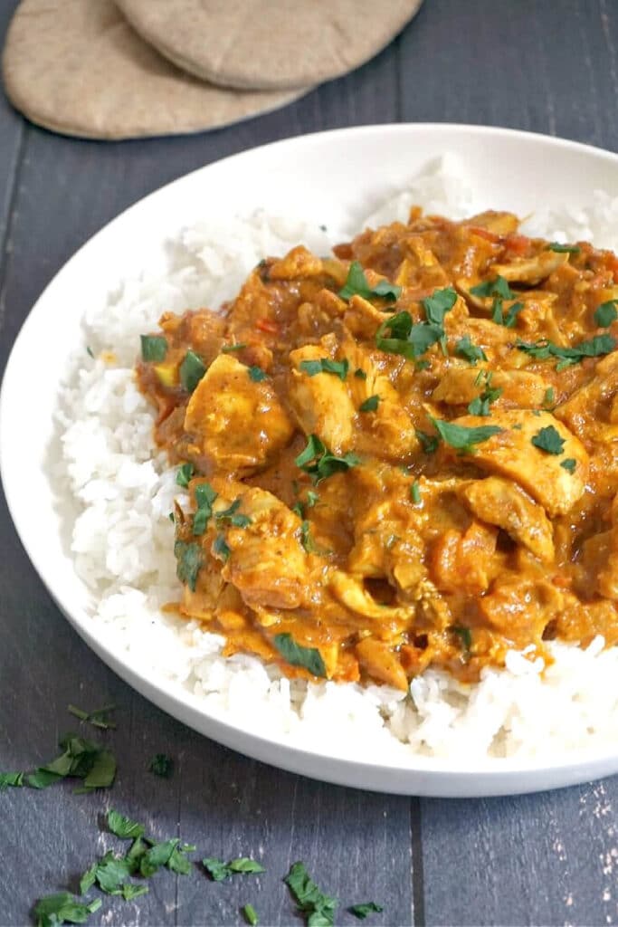 A white bowl with chicken curry over a bed of rice