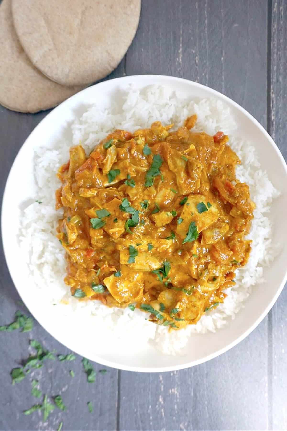 Overhead shoot of a white plate with chicken curry over a bed of rice.