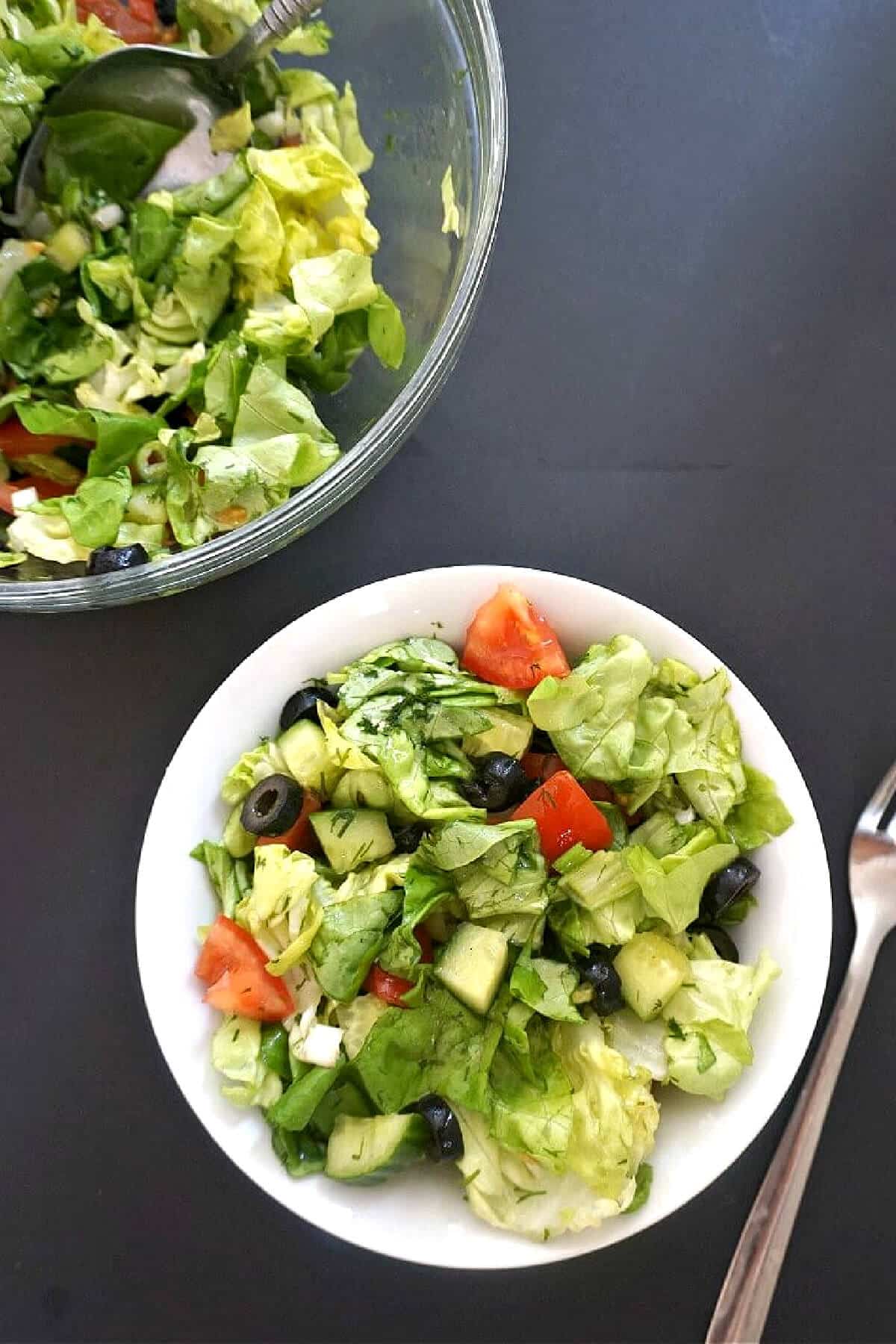 Overhead shoot of a white bowl with green salad and a bowl with more salad.