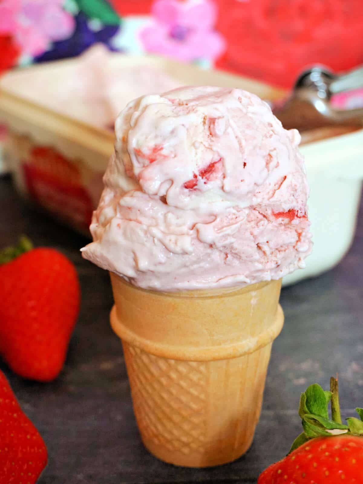 A cone with a scoop of strawberry ripple ice cream with fresh strawberries around