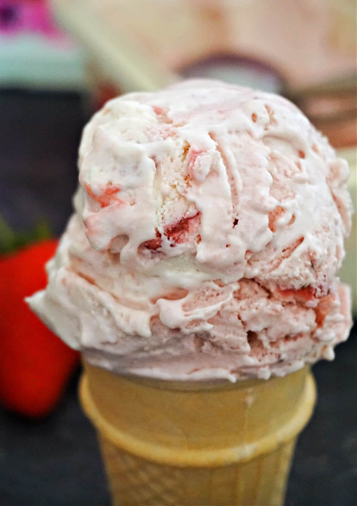 Close-up shot of a cone with a scoop of strawberry ripple ice cream.