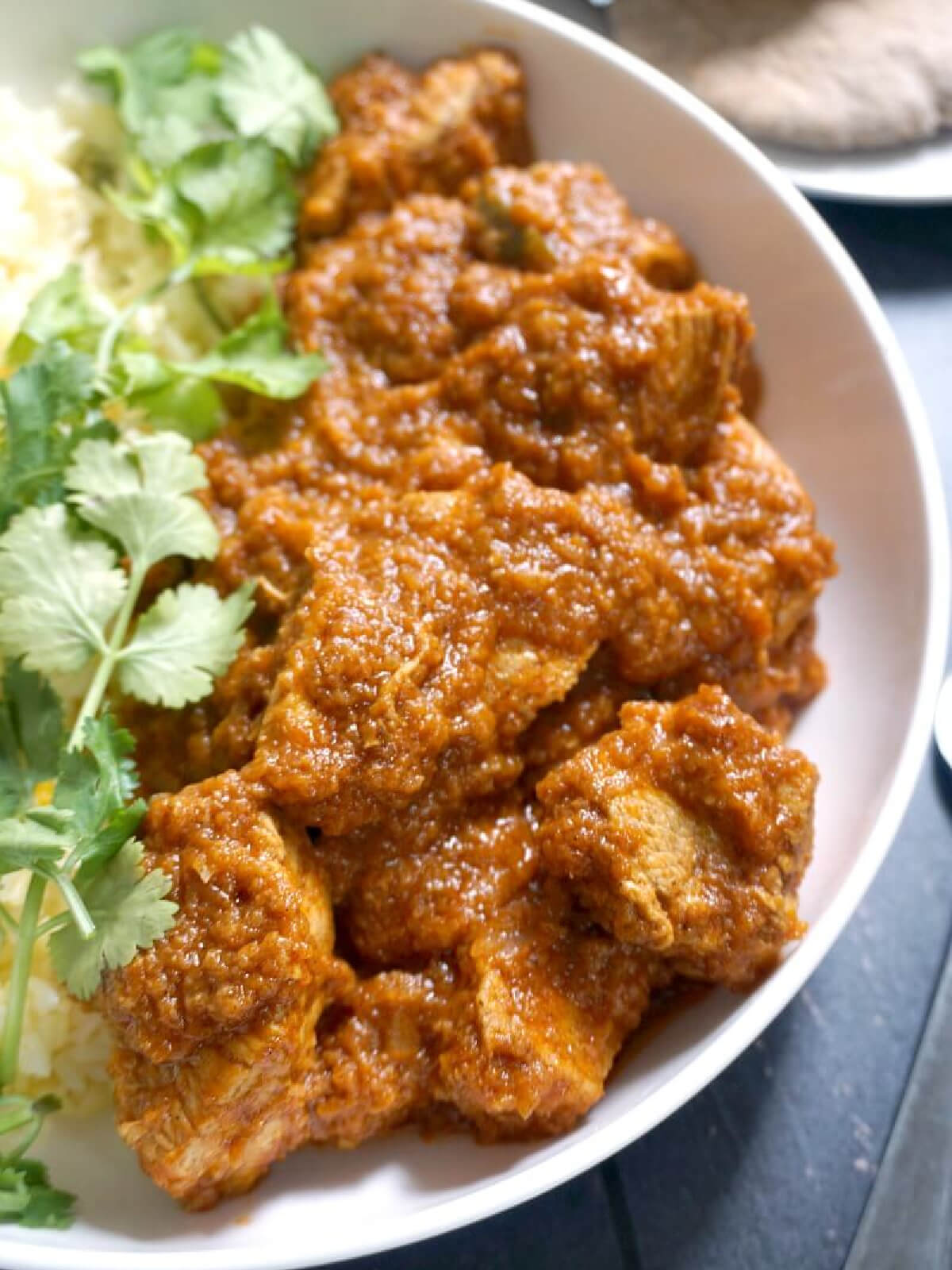 A white bowl with chicken curry and coriander leaves