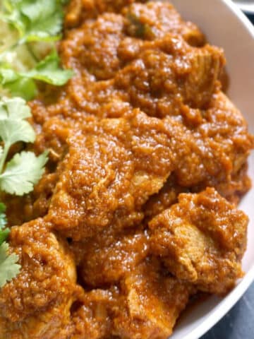 A white bowl with chicken curry and coriander leaves