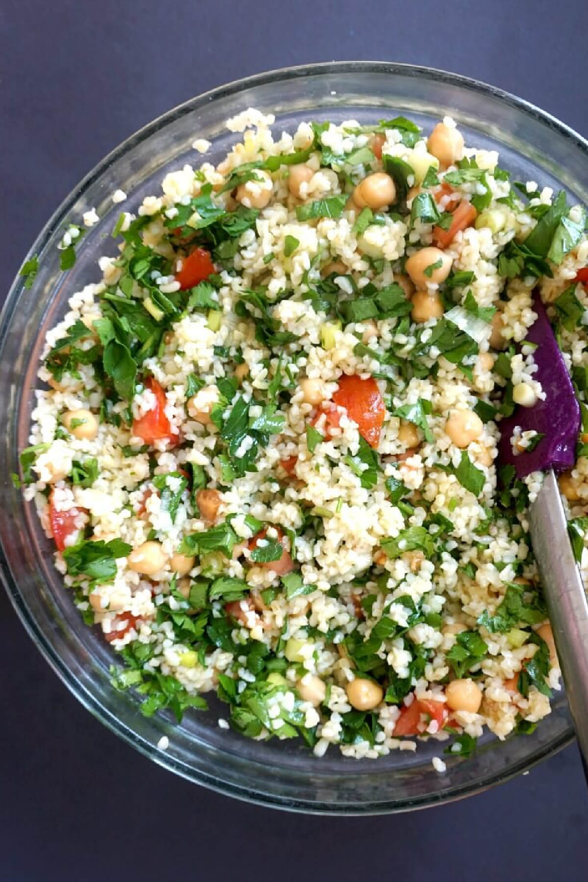 A glass bowl with tabbouleh salad and a spatula.