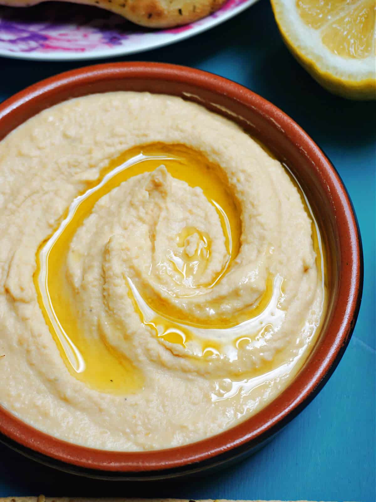 Close-up shoot of a brown ramekin with hummus with a whirl of olive oil on top.
