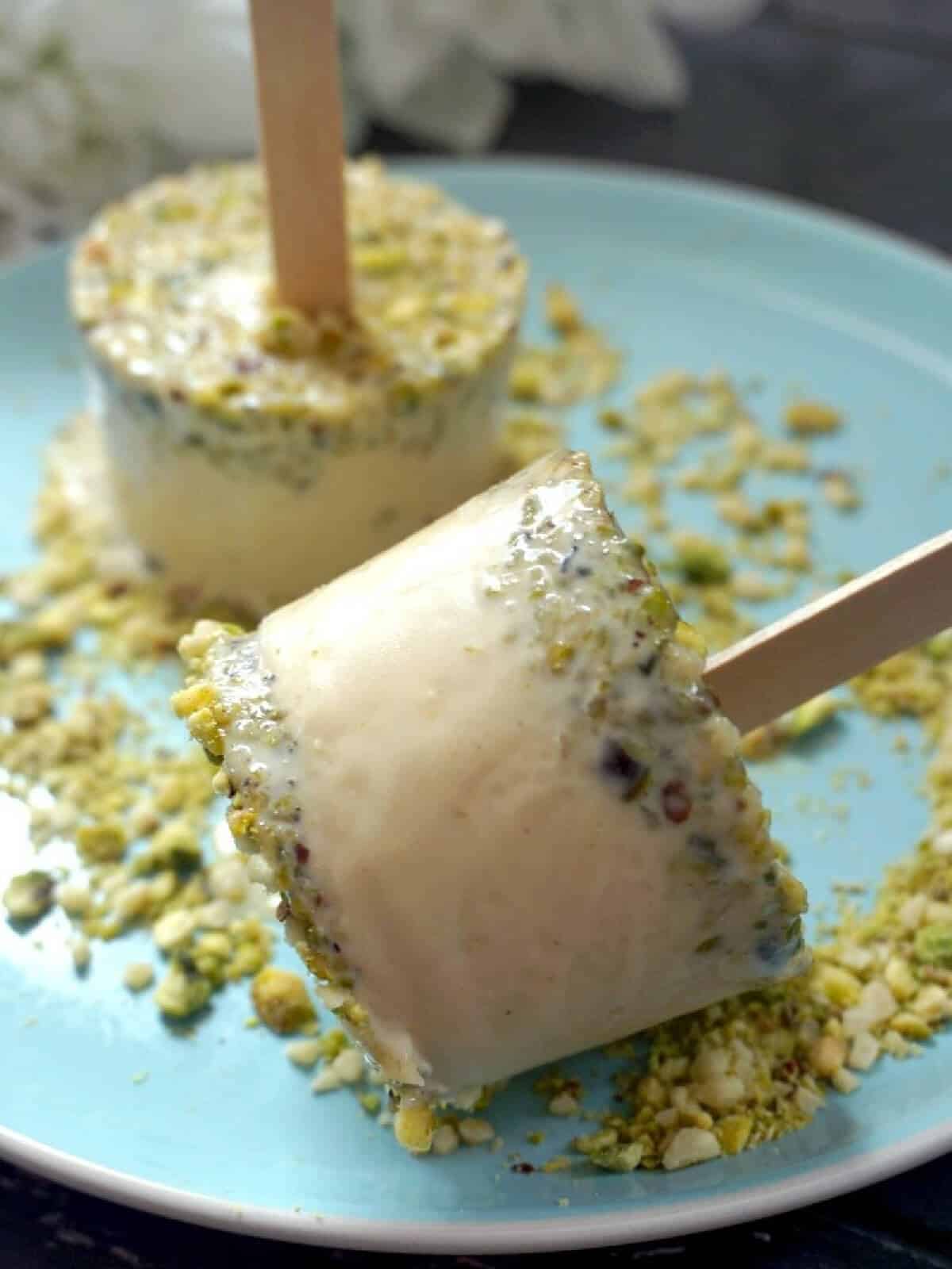 2 kulfi ice creams on a light blue plate with chopped pistachio.