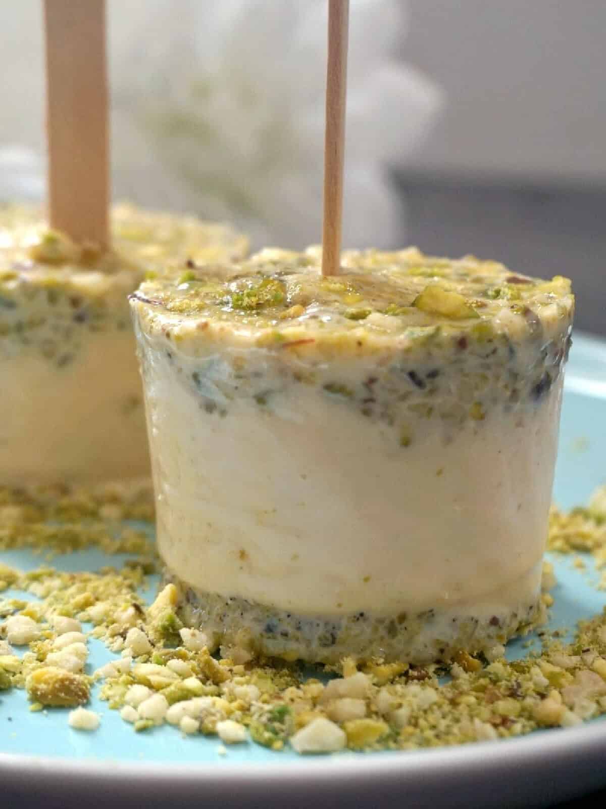 2 kulfi ice creams on a bed of chopped pistachios.