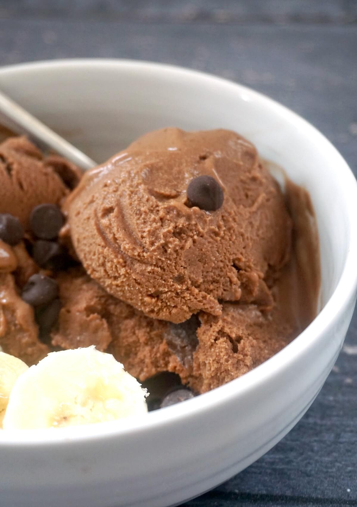 A white bowl with chocolate ice cream, slices of bananas and chocolate chips