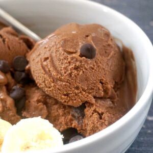 A white bowl with chocolate ice cream, slices of bananas and chocolate chips