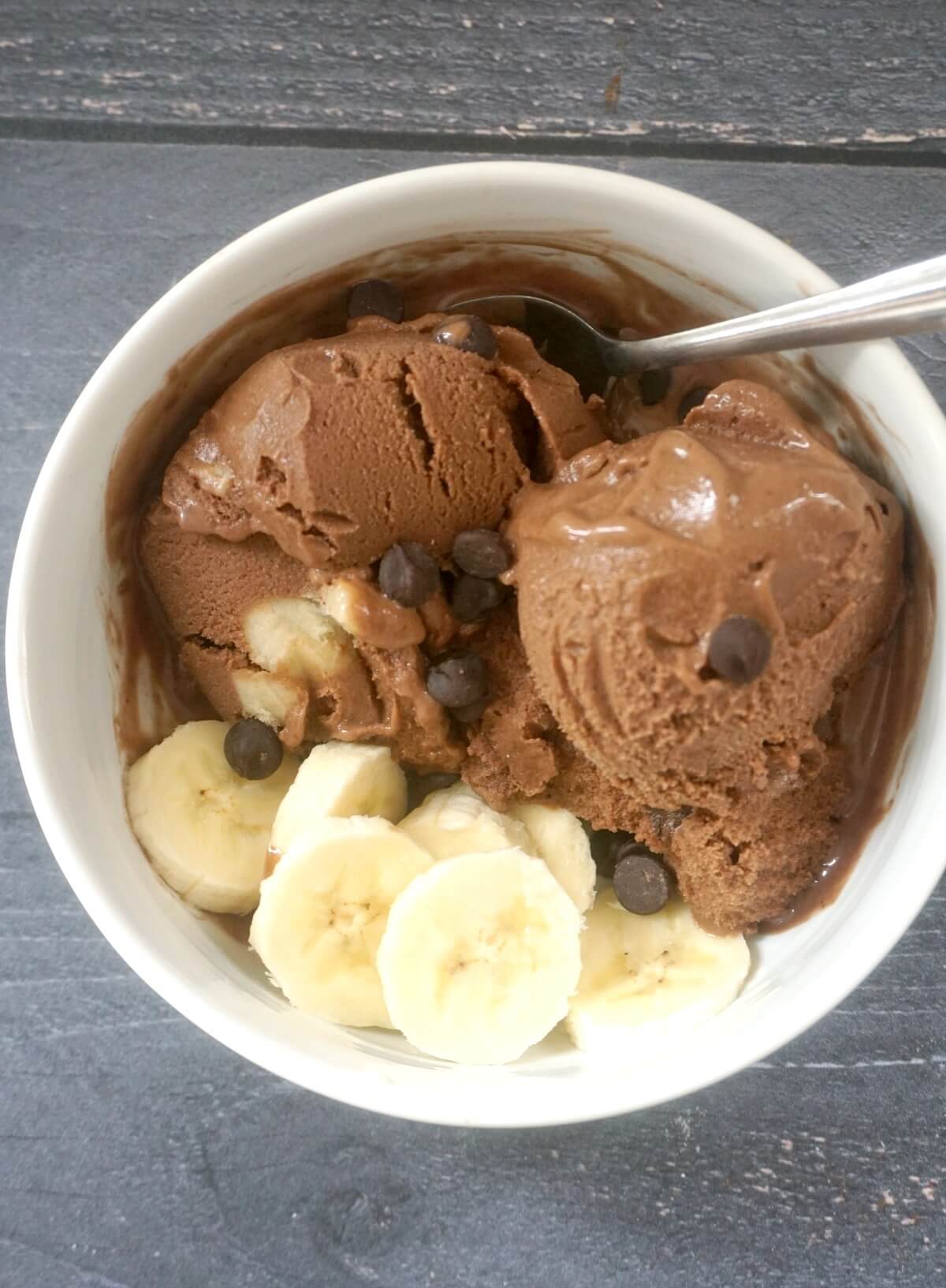 Overhead shoot of a white bowl with ice cream, slices of bananas and chocolate chips
