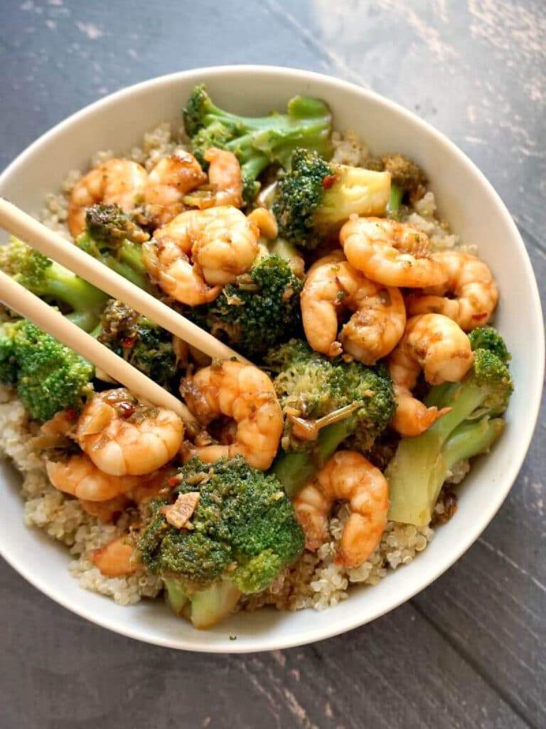 A white bowl with shrimp and broccoli over a bed of couscous
