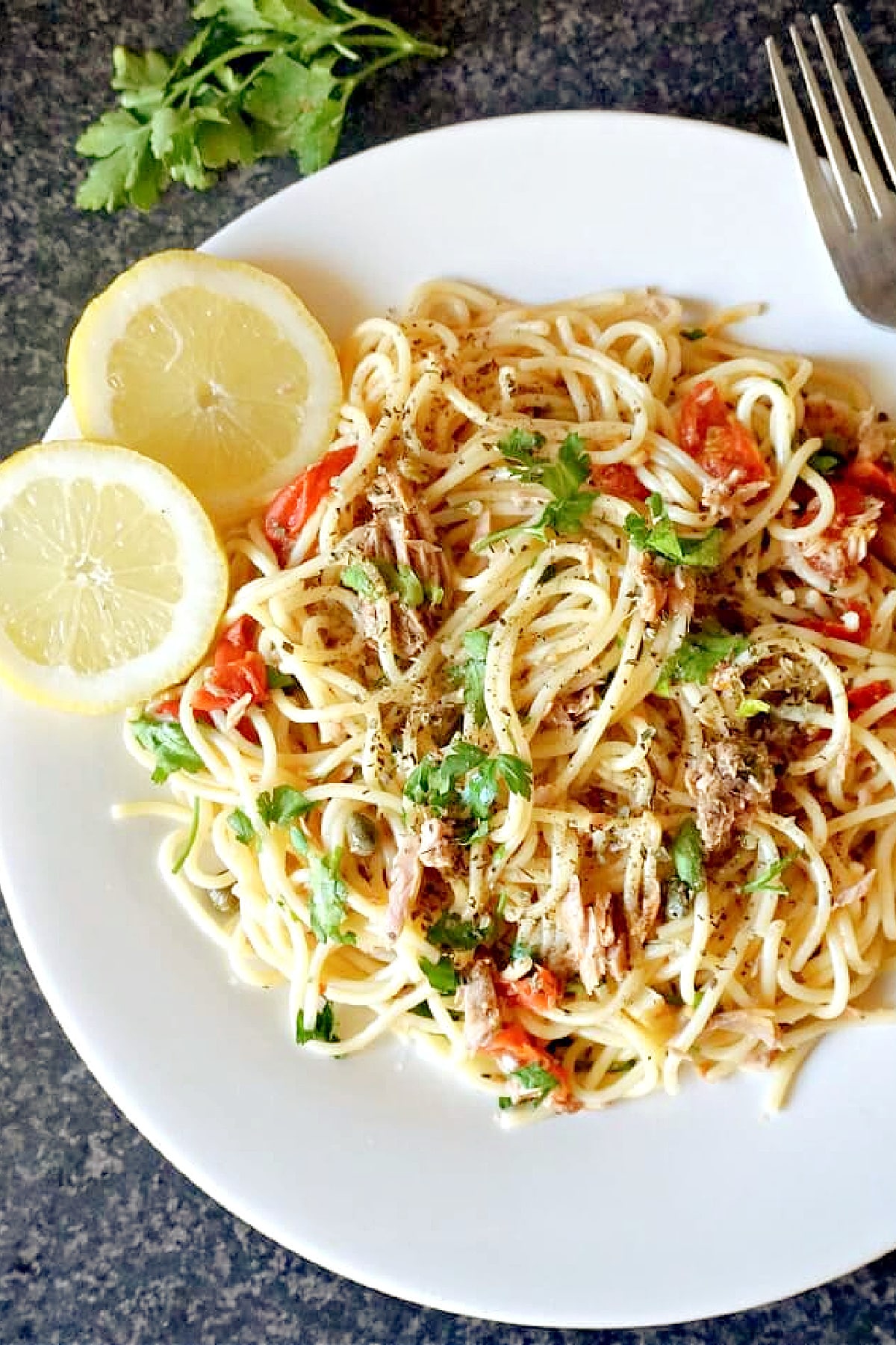 Overhead shoot of a white plate with spaghetti with tuna, and 2 slices of lemon on the side.
