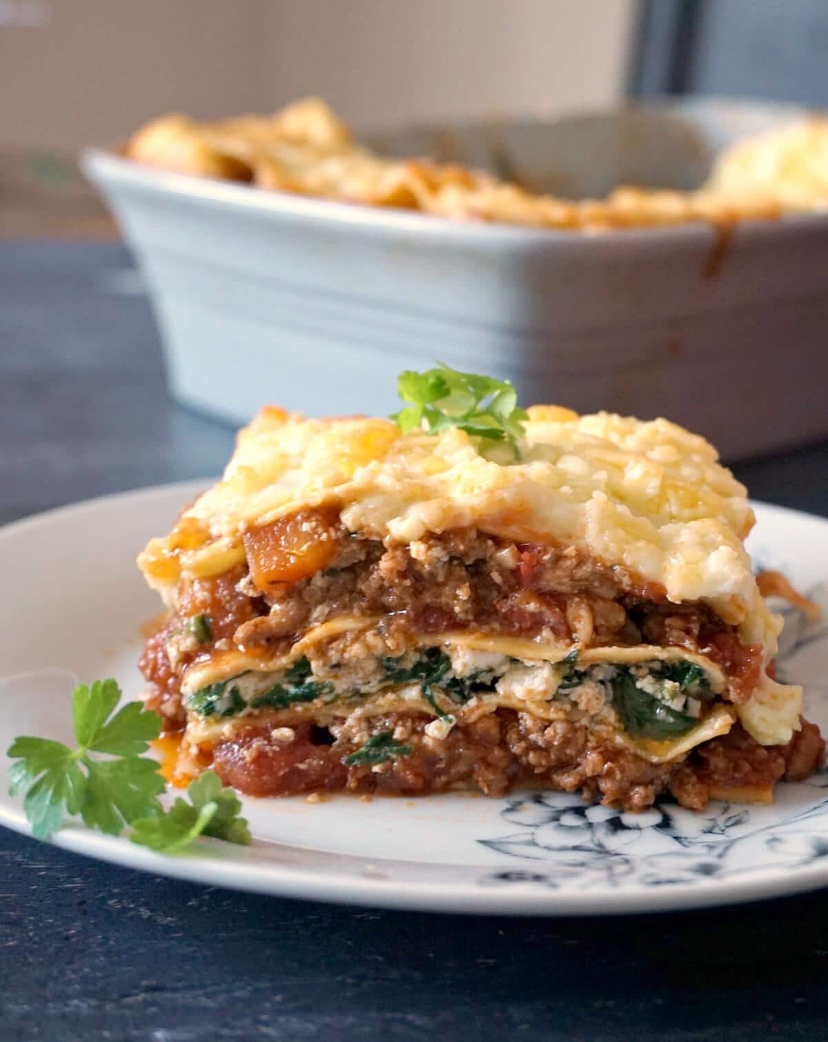 A slice of lasagna on a white plate garnished with fresh parsley leaves.