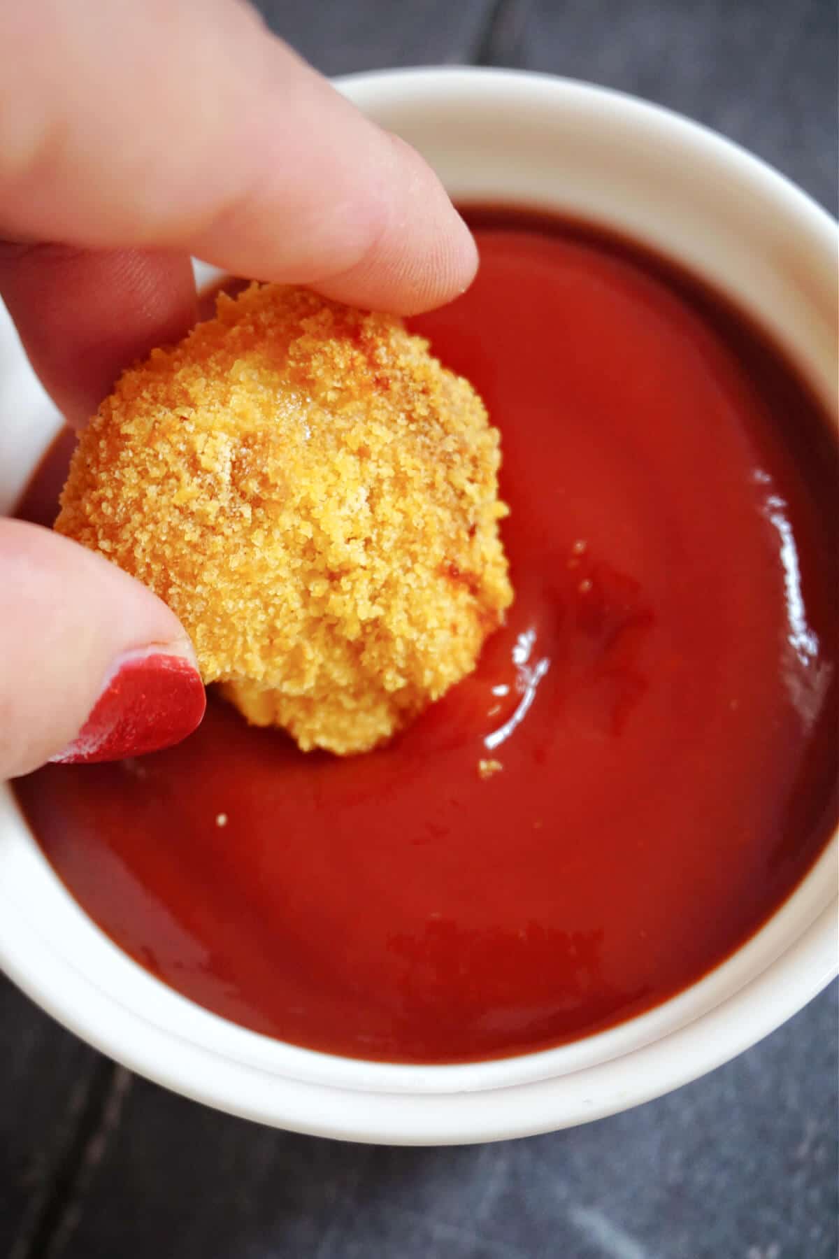 A chicken nugget being dipped in ketchup.