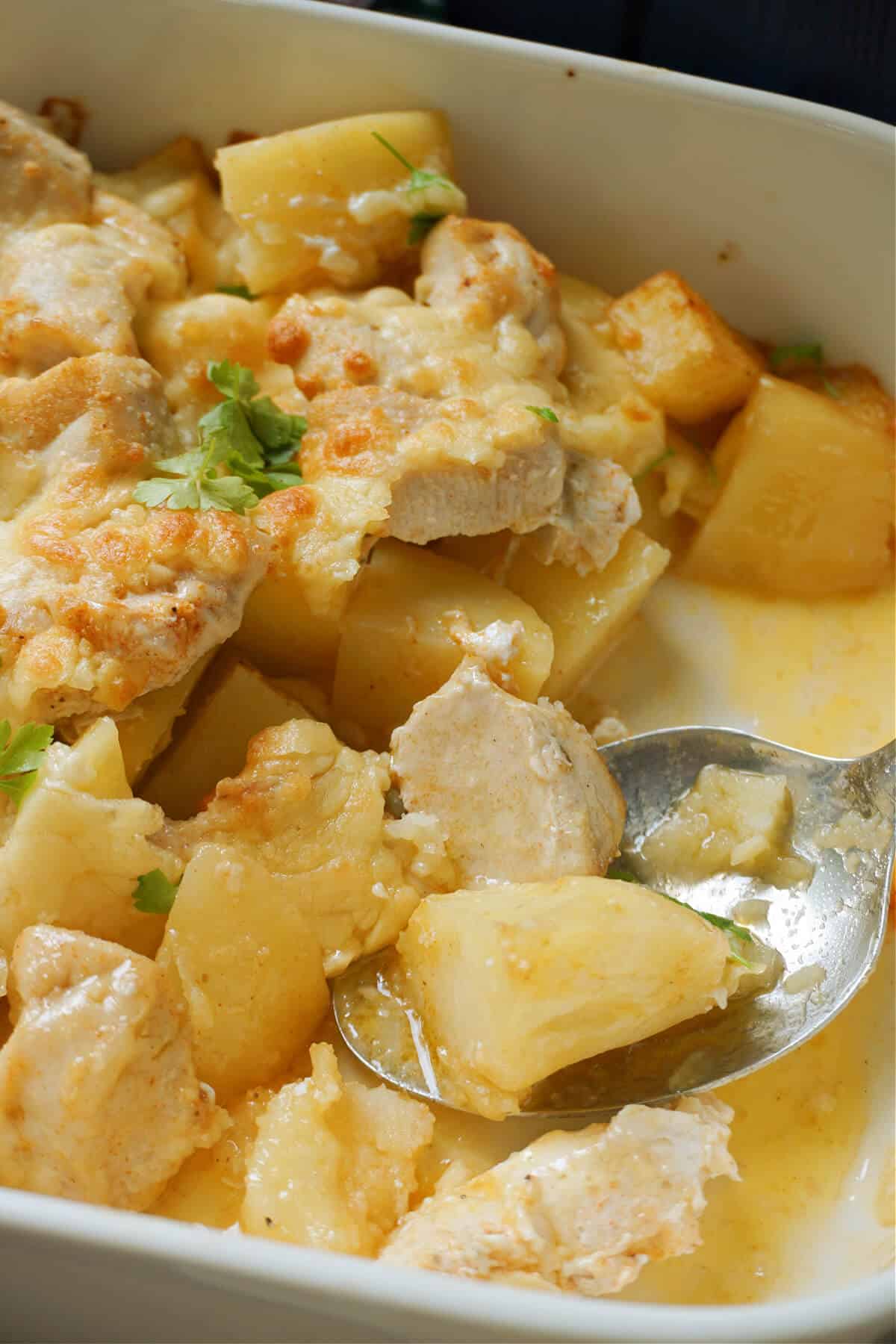 A dish with chicken and potato pieces and a spoon in it.